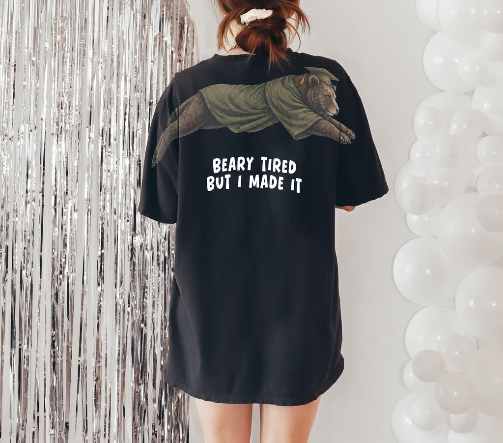 Bear Beary Tired But I Made It graduation graphic tee by Dripvity, unisex oversized white t-shirt with leaping bear in graduation cap and gown