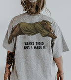 Bear Beary Tired But I Made It graduation graphic tee by Dripvity, unisex oversized white t-shirt with leaping bear in graduation cap and gown
