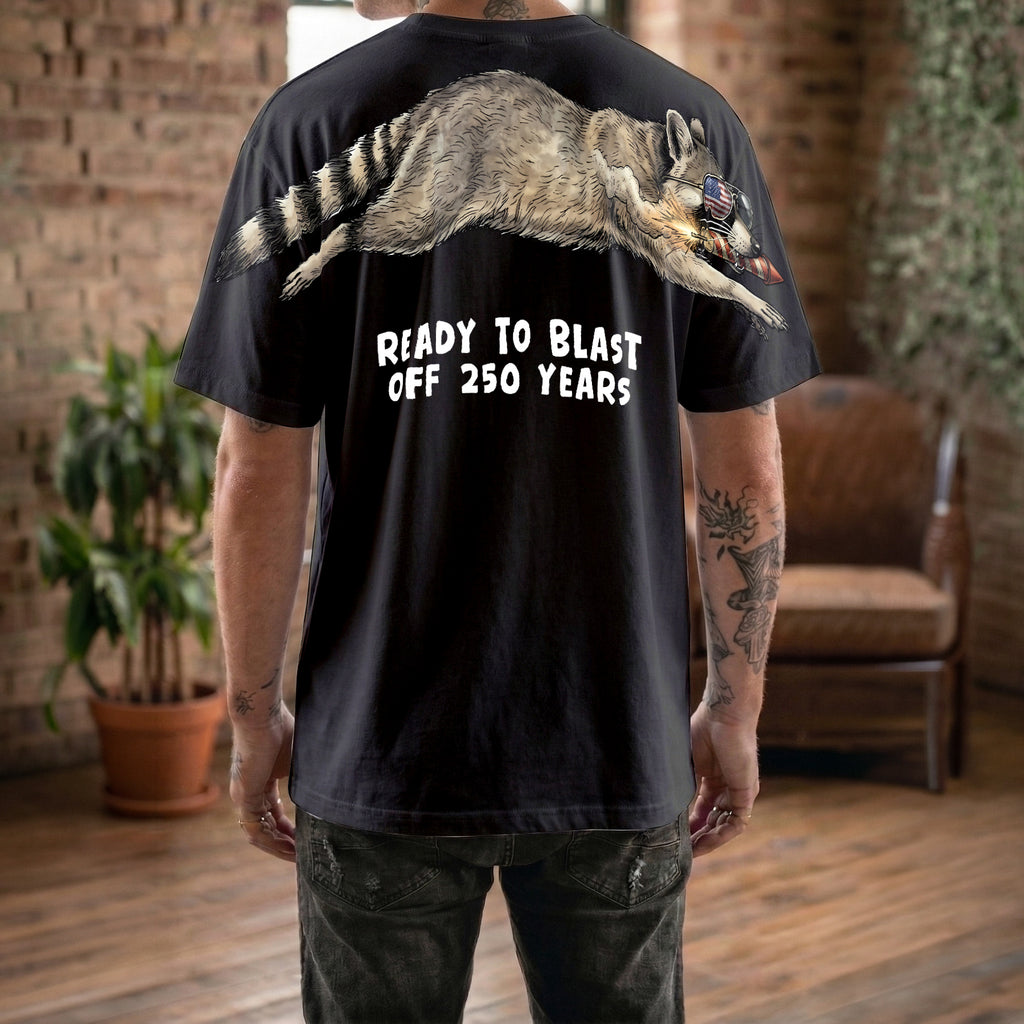 Raccoon ready to blast off 250 years graphic tee by Dripvity, unisex oversized black t-shirt with patriotic raccoon and fireworks design