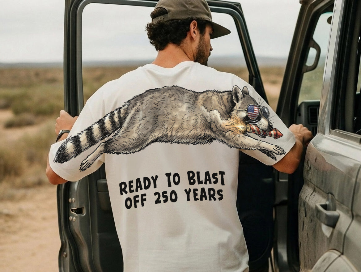 Raccoon ready to blast off 250 years graphic tee by Dripvity, unisex oversized black t-shirt with patriotic raccoon and fireworks design