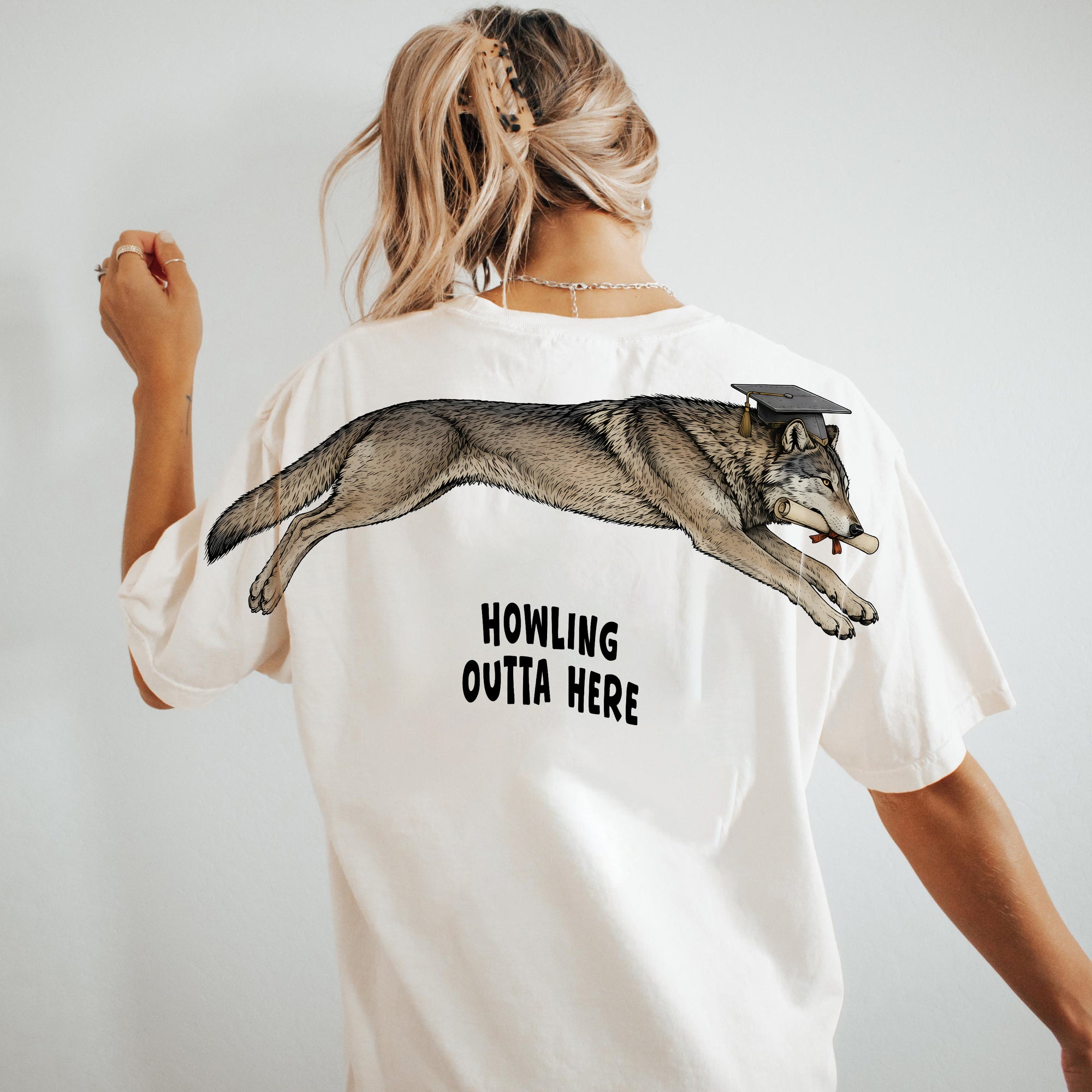 Wolf Howling Outta Here graduation graphic tee by Dripvity, unisex oversized white t-shirt with leaping wolf in graduation cap and diploma